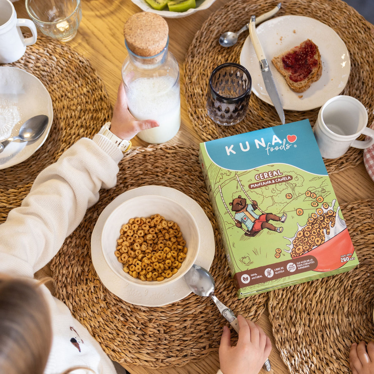 Caja Cereal Manzana Canela Kuna Foods, cereal en caja sin azúcar añadida, con tono verde y mesa de desayuno