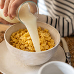 Caja Cereal Vainilla Kuna Foods en tazón blanco con cereales dorados y leche vertiéndose
